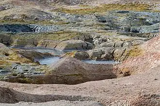 A pool of greyish-blue bubbling sludge surrounded by rocks and steam