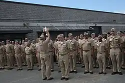 A sailor holds up a trophy in front of a formation of sailors