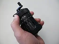 A person's hand is holding a small, metallic cylinder with a crank sticking out.