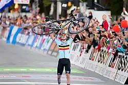 Remco Evenepoel holds his bicycle above his head after crossing the finish line