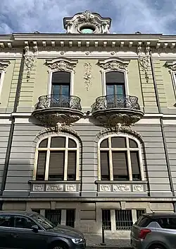 Complex wrought iron papo-de-rola balconies with elaborate Rococo Revival shells and round shapes (aka volutes) under them, on the facade of Strada General H. M. Berthelot no. 41, Bucharest, unknown architect, 1911[58]