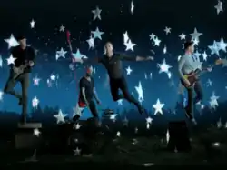 Coldplay floating in the air with their respective instruments, assisted by cables