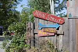 "A series of signs nailed to a wooden fence. They include the following: a red sign that reads Main Street, a blue arrow pointing right, and a pink sign that says Mayor Stubbs with an arrow pointing in the same direction. Mayor Stubbs is a cat that people like to say runs the town."