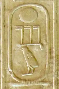 Three hieroglyphs inscribed on a cream-colored stone: a circle, beneath it three toes and a chick