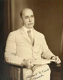 Cook seated in a wooden armchair holding a book