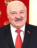 A older man partially smiling with short white hair, a grey mustache, and a black suit