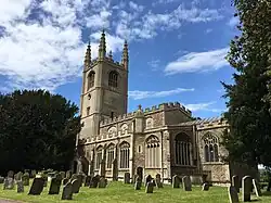 A stone church seen from the southeast with Perpendicular windows, embattled parapets, and a west tower with tall pinnacles