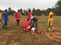 an injured player lies in the grass while several teenaged players look on