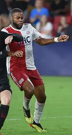 A soccer player is running next to another soccer player who is out of frame.