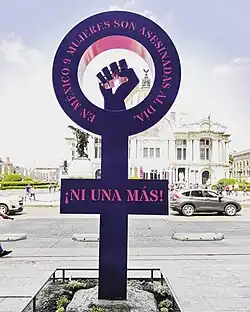 A symbol of Venus with a closed fist raised in the center. It has inscribed the phrases "In Mexico, 9 women are murdered every day" and "not a single one more!" in Spanish.
