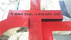 A large plus symbol with Spanish writing on it, stating "A una voz, ¡rescate ya!".