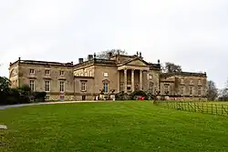 A mansion with two adjacent wings, with a gravel drive and lawn in front