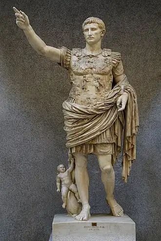 This image shows the sculpture Augustus of Prima Porta, a full body portrait of the Roman Emperor Augustus. He is depicted wearing armor that shows the story of one of his diplomatic gains as well as with a small cherub and dolphin by his right leg.