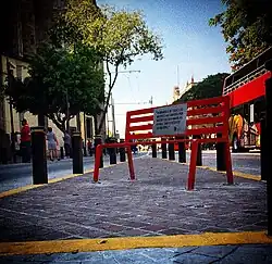 A red bench with a plaque that reads "In memory of all the women murdered by those who claimed to love them or just because they were women" in Spanish.