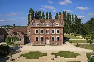 Red brick house with a single storey section to the left, and trees to the right