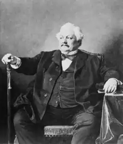 Middle-aged corpulent white man with white moustache and full head of white hair, seated