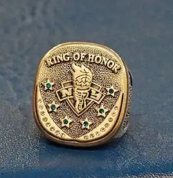 A gold ring with the words quote ring of honor" at the top six stars with jewelsin the symbol of the New York Liberty in the center