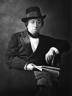Disraeli in old age, wearing a double-breasted suit, bow tie and hat