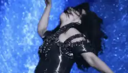 Whilst wearing a shimmering black outfit, Björk is shown twirling her arms while blue lava erupts behind her