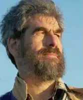 Head of man in heroic pose, viewed from below, aged around 50 years with greying dark hair, bushy eyebrows, full beard, and strong facial features