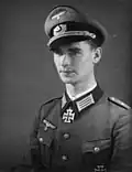 A man wearing a peaked cap and military uniform with an Iron Cross displayed at the front of his uniform collar.