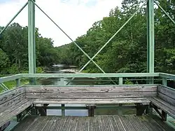 A detail of the wooden seat and observation platform at the center of the green Whipple truss bridge facing out over a river