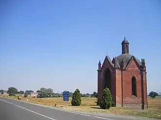 Photo of a small brick chapel on a highway amid rolling pastures. A sign reads Voghera to the right and Piacenza to the left.