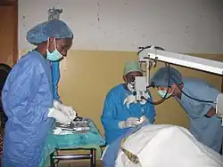 Surgeon using surgical microscope to operate while theatre staff attend.
