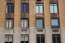 View of some windows on the third to fifth stories. There are notches at the tops of each cast stone pier. Above are vertical brick piers, as well as windows separated horizontally by darker curved spandrel panels.