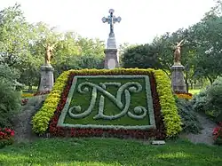 Floral display at the cemetery, with "NDC" on raised bed, cross and two statues of angels in the background