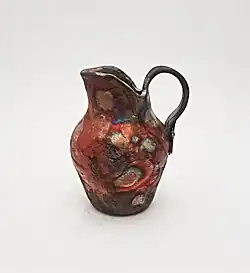 Made by Ruthann Hurwitz (The Village Potter) in the Western style of Raku. It was built with the coil and pinch method, glazed, then fired. It was removed from the 1800 degree kiln while red hot and placed into containers with combustibles, then covered where reduction takes place, "smoking" the pottery.
