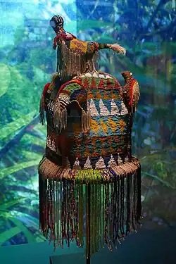 Yoruba type royal crown, Ade Nla from the kingdom of Danhomè, a kingdom that developed under heavy cultural influence from its much larger Yoruba neighbor. The beaded veil shields the Oba's own face and transforms him into a living embodiment of Odùduwà and the force of the collective ancestors. The birds signify that the Oba is a divine ruler. Half in the physical and half in the spiritual realms just as the birds can traverse both the terrestrial and the celestial. Musée du Quai Branly