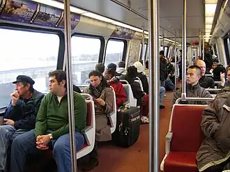 Passengers sit in fixed two-seat units. There are metal poles and bars for standees to hold.