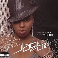 Jaguar Wright, wearing a black hat, rests her hand on her left shoulder