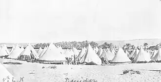 a large group of light-coloured cone-shaped tents in a desert setting
