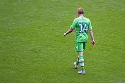 A colour photograph of Kevin de Bruyne, face back to the camera, wearing an all-green kit.