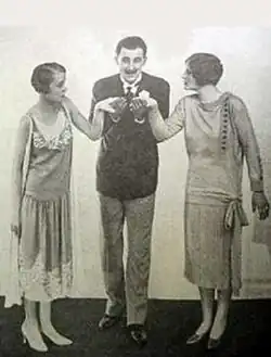 smart youngish man in blazer, kissing the hands of two youngish women either side of him