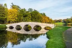 A bridge with five arches, which appears to be made of off-white stone, crossing a water channel with a white folly on the hillside in the far distance.