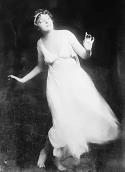A white woman wearing a white flowing dress, dancing against a dark background