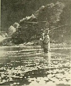A man wearing waders, standing thigh deep in the river casting a flyrod