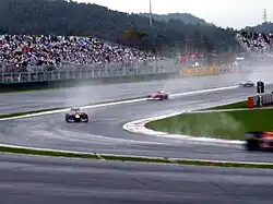 Four Formula One cars are turning left into a corner with spray being lifted from the ground by their tyres.