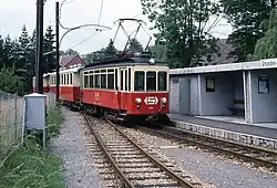 Single-car electric railcar pulling two passenger carriages with open balcony ends