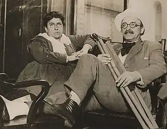 A woman and man in their 40s, sitting. The man's ankle is elevated and he is carrying crutches