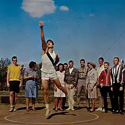 A photo of a teen who has just thrown a shotput and is surrounded by onlookers