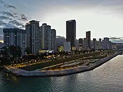 Aerial view of a seafront park, with skyscrapers forming the backdrop.