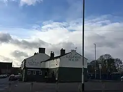 Photo of the Halfway House pub, Stanningley Leeds, showing the painted inn name on the end and side of the pub, with a cloudy and blue sky above