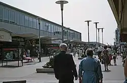Pedestrians walking through a wide area between shop fronts