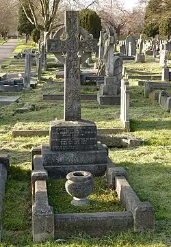 A granite headstone surmounted by a Celtic cross, among several other gravestones