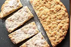 A round streuselkuchen, cut in pieces. Half the cake has been dusted with powdered sugar