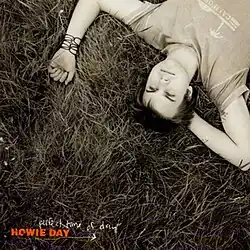 Howie Day lays in the grass with a neutral look on his face. The cover is sepia-toned. Day is wearing a shirt that says "California" and a black bracelet. On the bottom left of the cover, the word HOWIE DAY is capitalized and orange while perfect time of day is lowercase and white.